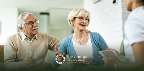 An elderly couple talking to a caregiver in a memory care facility