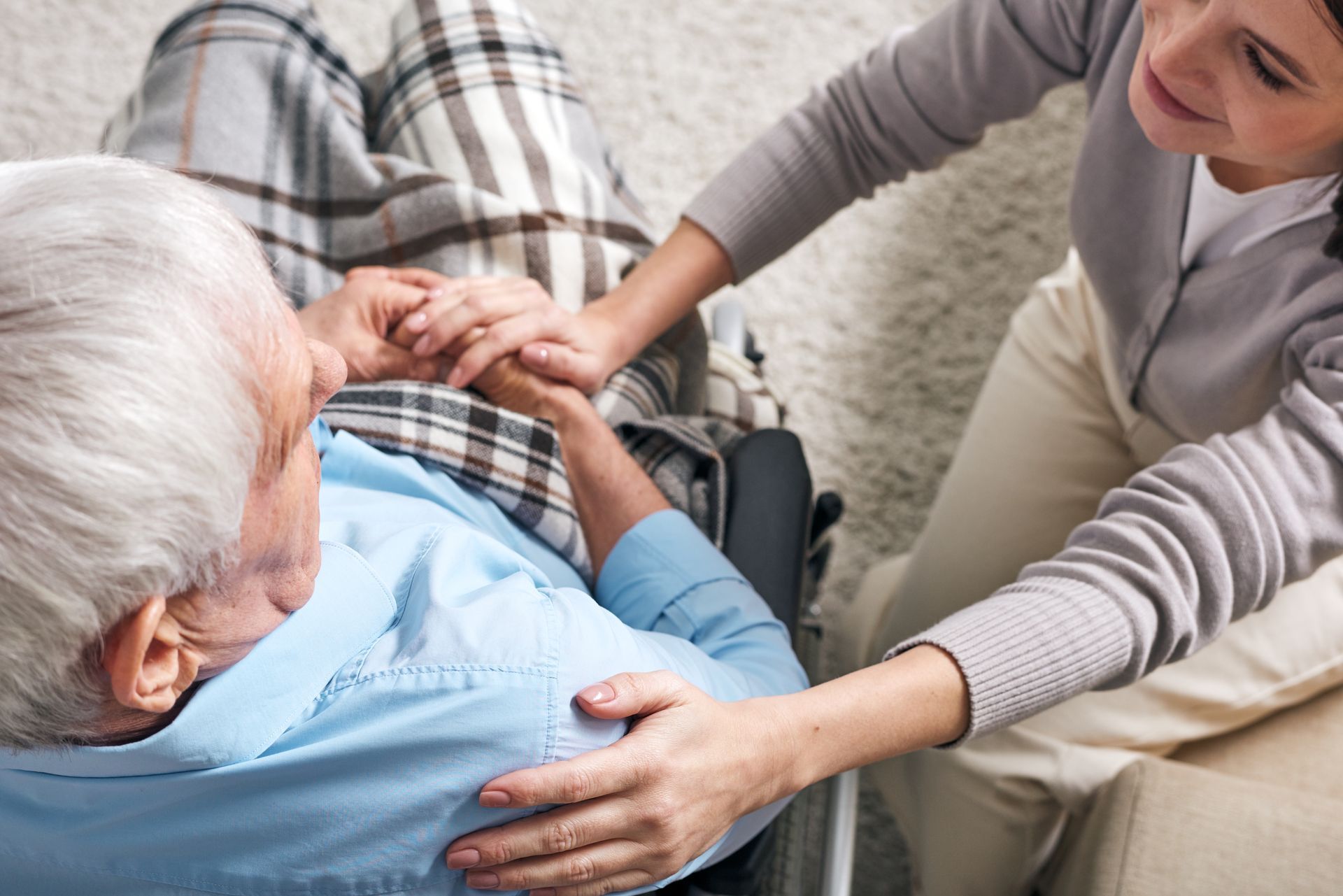 A woman is holding the hand of an elderly man in a wheelchair.
