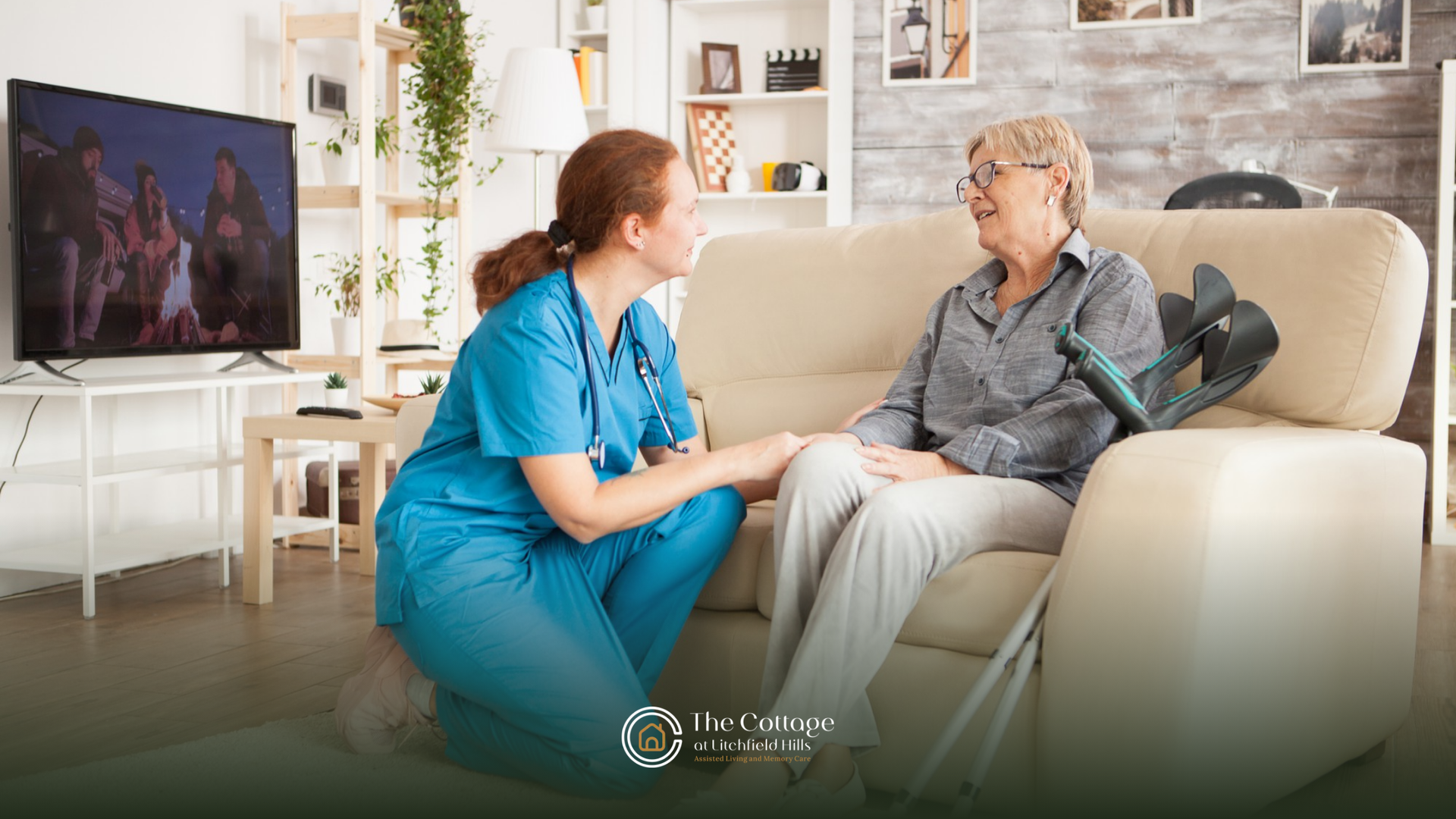 A nurse is kneeling next to an elderly woman sitting on a couch.
