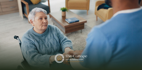An older person in a wheelchair holds hands with her caregiver.
