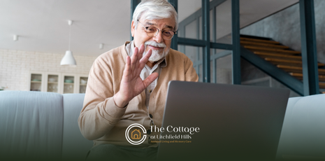 Older adult on a video call, waving from a laptop.