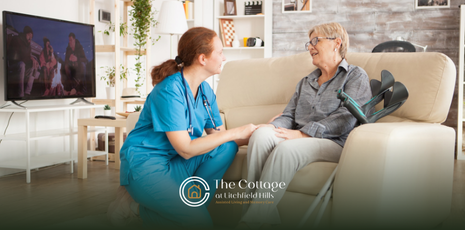 Nurse in blue scrubs talking to a seated older adult 