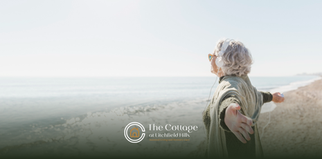 An elderly woman with arms outstretched by the ocean