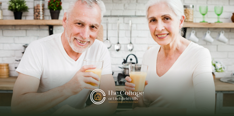 Two elderly adults drinking a glass of protein shake in a kitchen