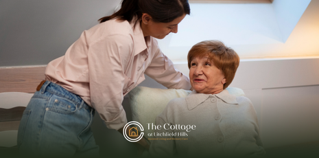 A caregiver assisting an elderly woman seated on a couch.