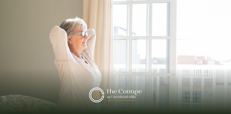 An elderly woman stretching by a window