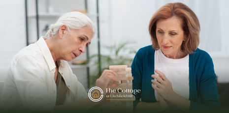 Two elderly women focused on playing a stacking block game together.