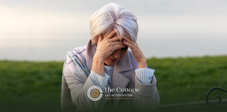 An elderly woman with hands on her face, appearing distressed outdoors. 