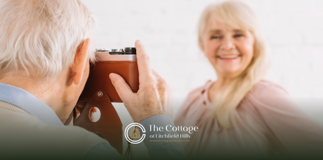 An elderly person is taking a photo of an elderly woman. They are both smiling.