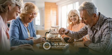 A group of seniors smiling, enjoying snacks and drinks around a table in a senior living community 