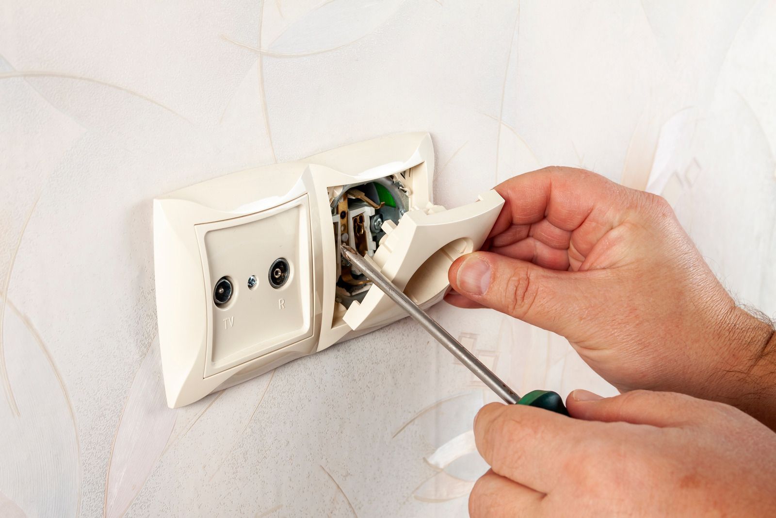 Hands using a screwdriver to remove a wall outlet cover on a patterned wall.