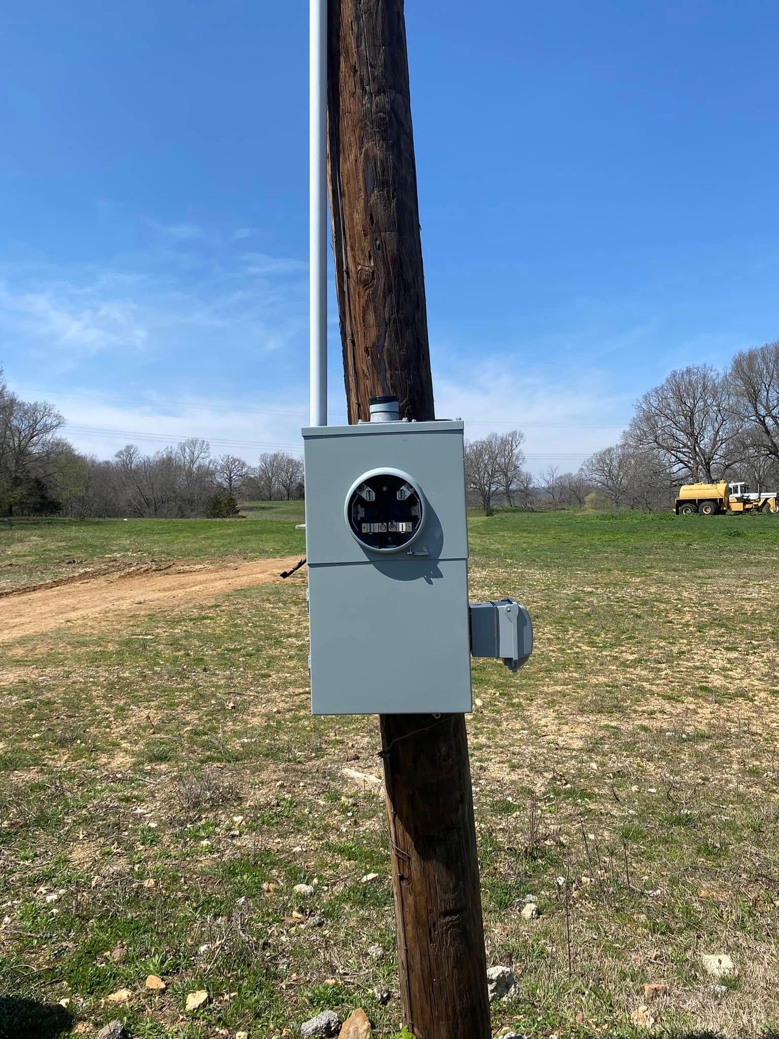 An electrical box is attached to a wooden pole in a field.