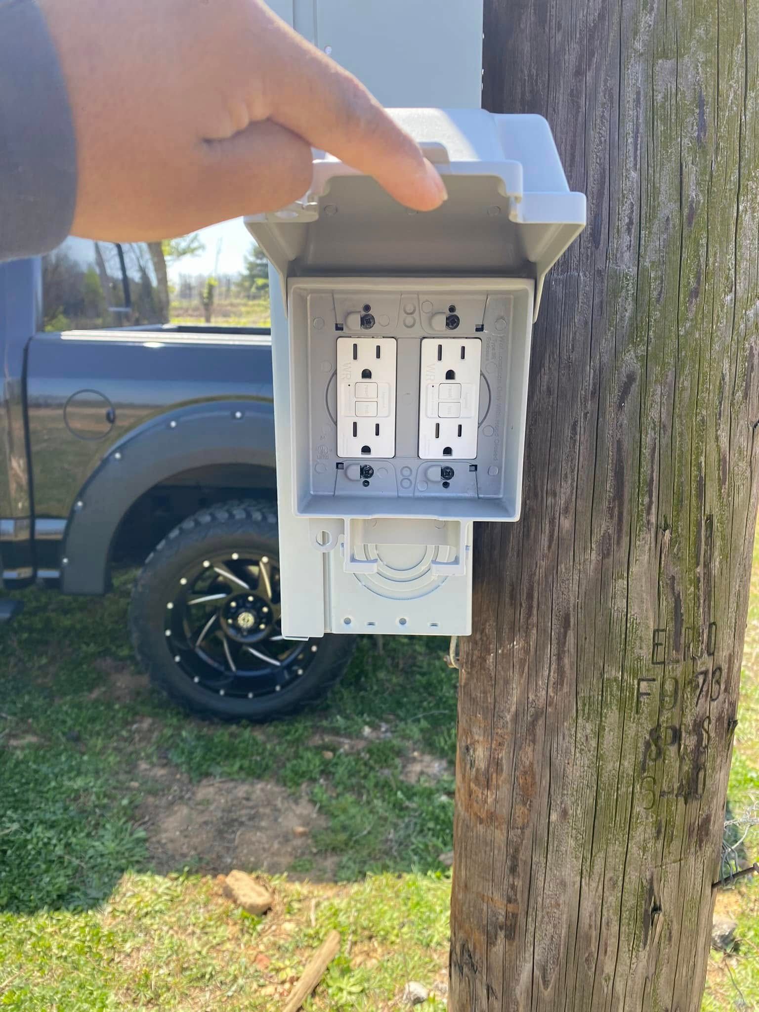 A person is pointing at a electrical box attached to a tree.