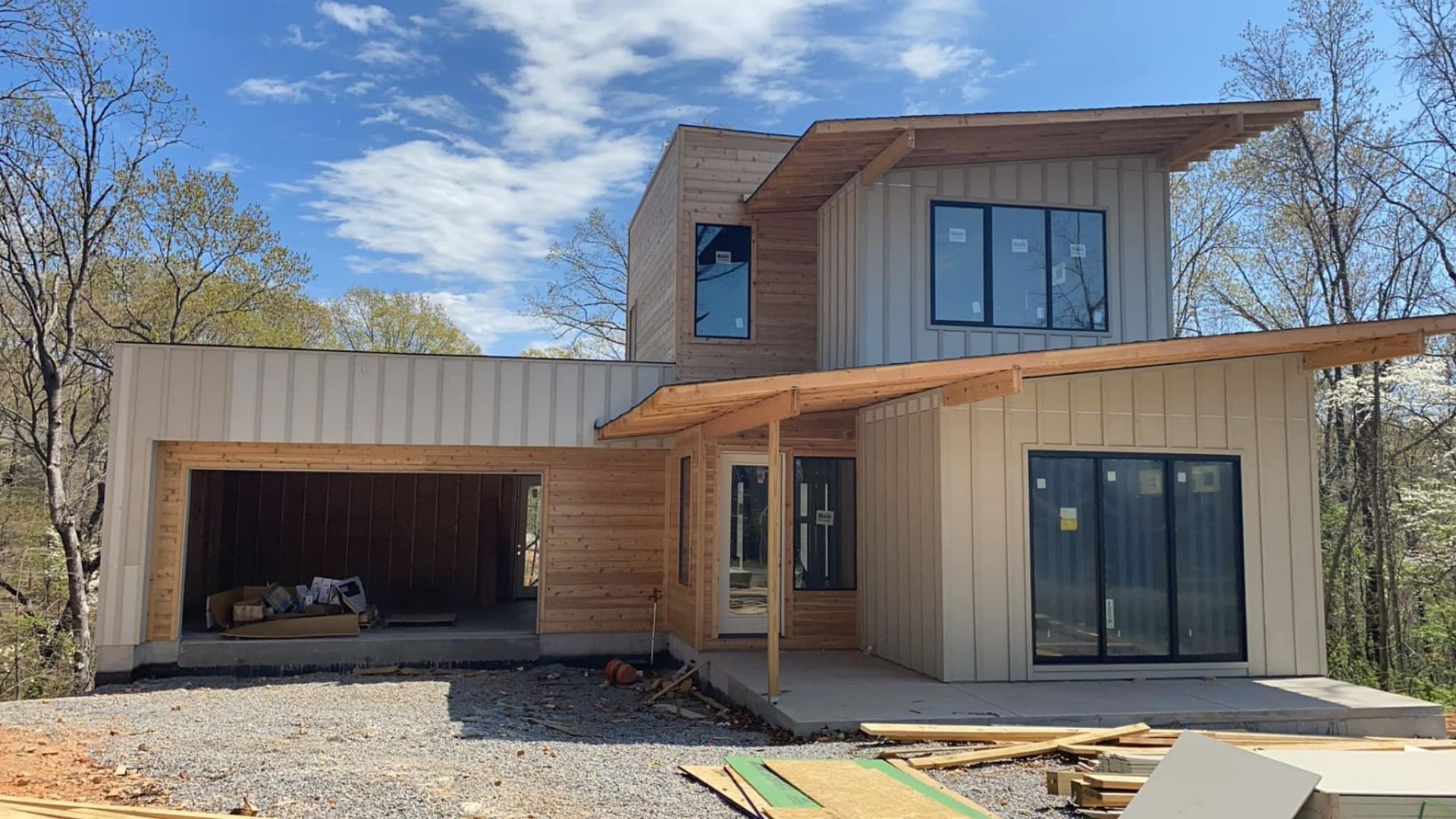A house is being built in the woods with a lot of windows and a garage.