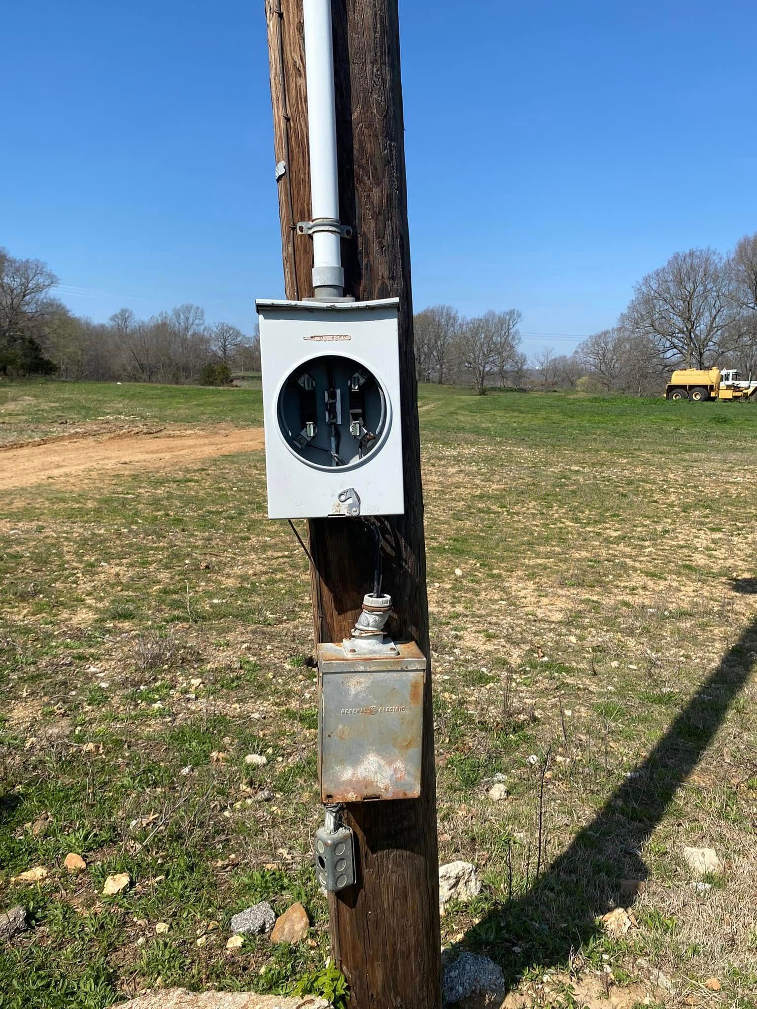 An electrical box is attached to a wooden pole in a field.