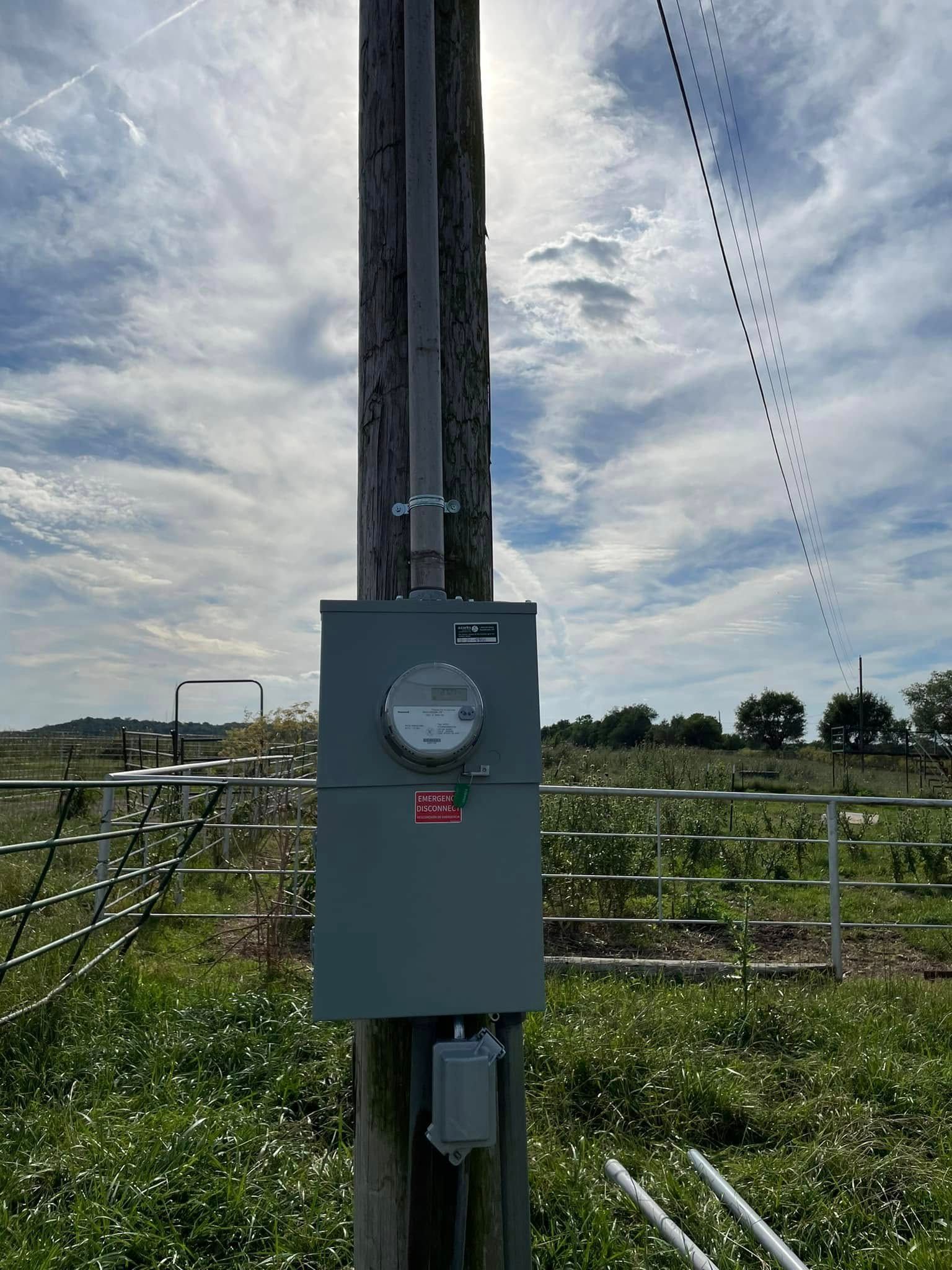 An electrical box is sitting on top of a wooden pole in a field.
