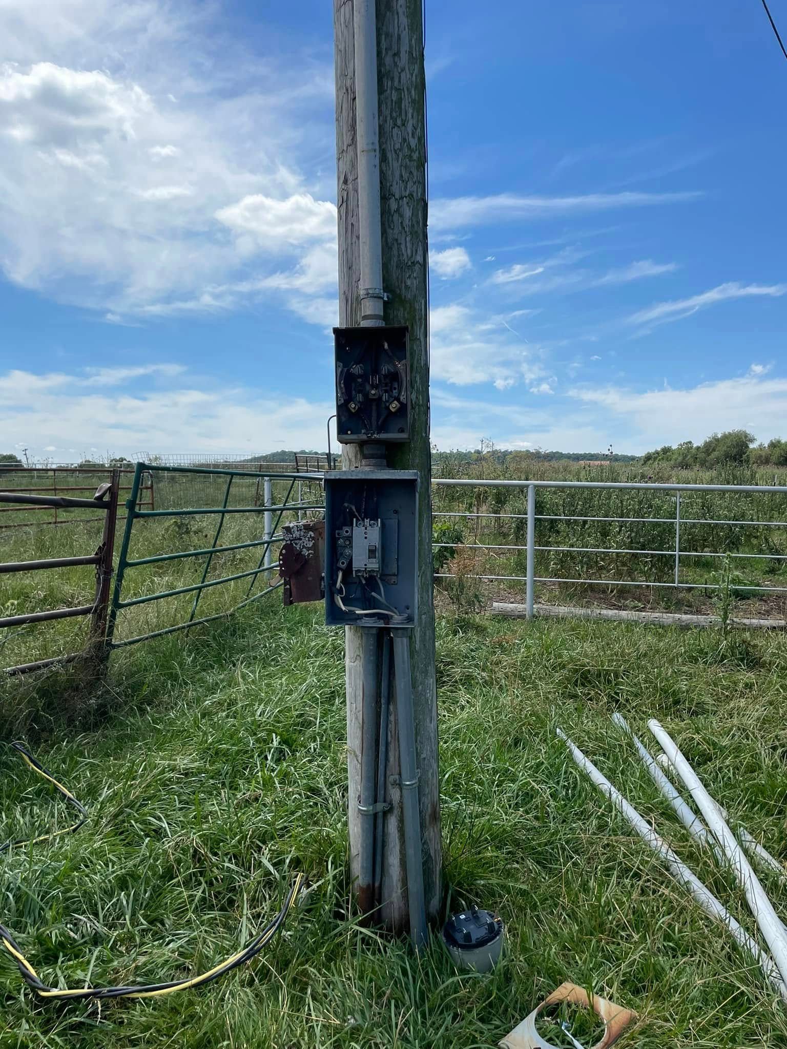 A wooden pole with electrical boxes attached to it in a grassy field.