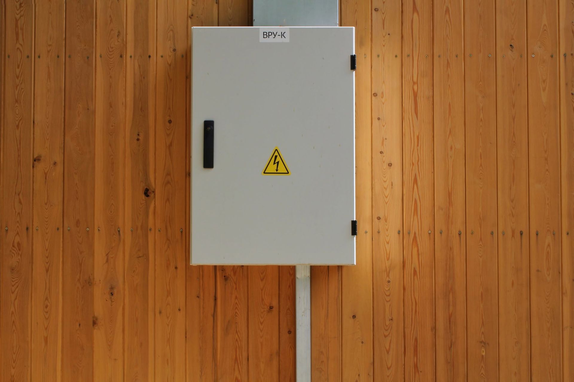 A white box with a yellow warning sign on it is attached to a wooden wall.