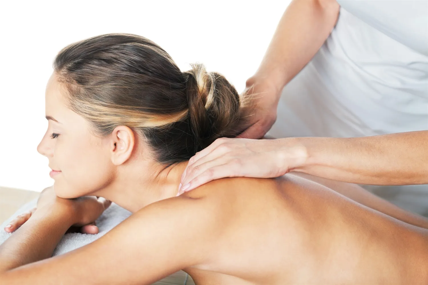 A person lies prone on a massage table while receiving a therapeutic shoulder and back massage from a practitioner.