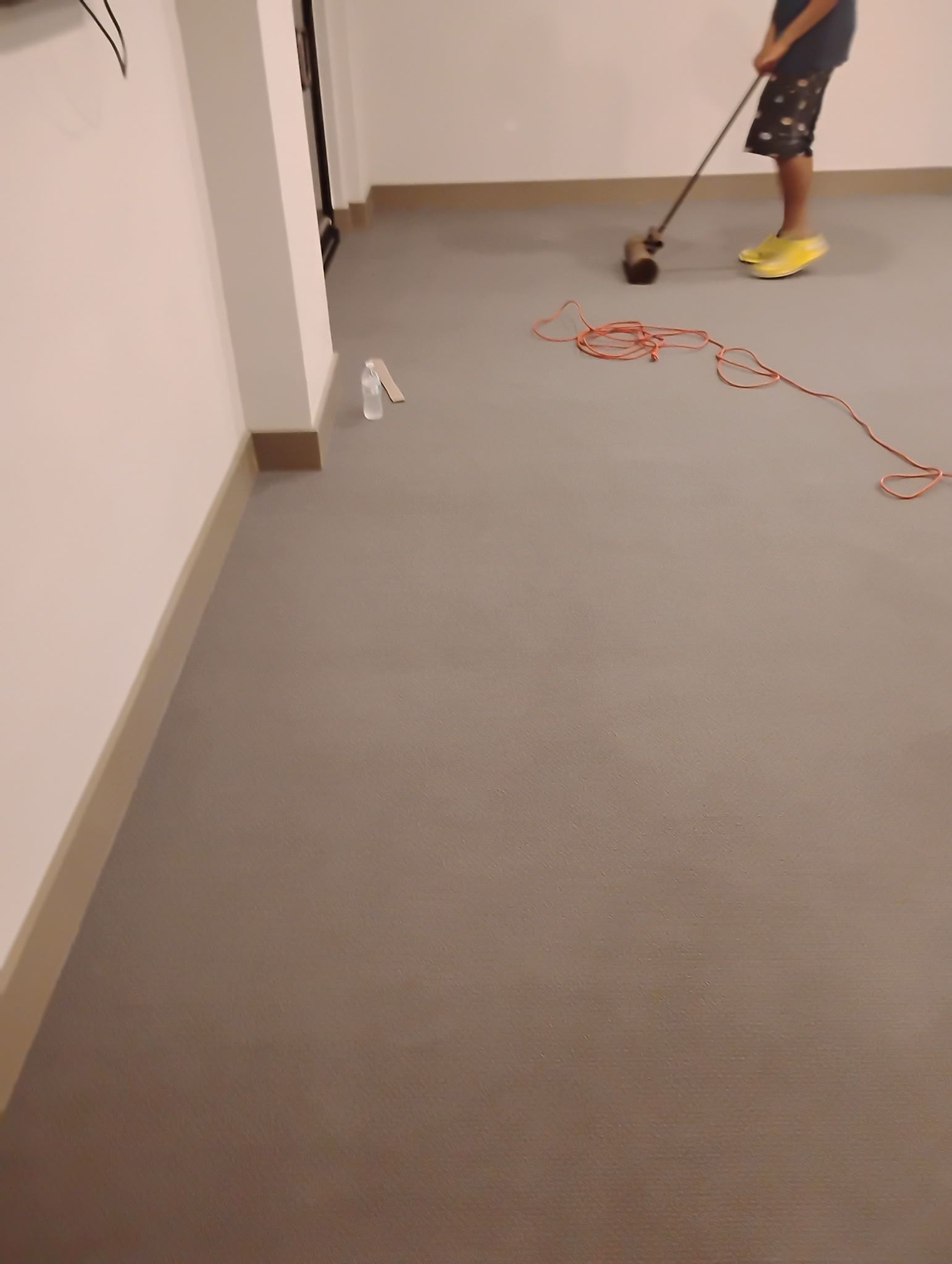Person cleaning a hallway floor with a vacuum, with an orange cord trailing across the carpet.