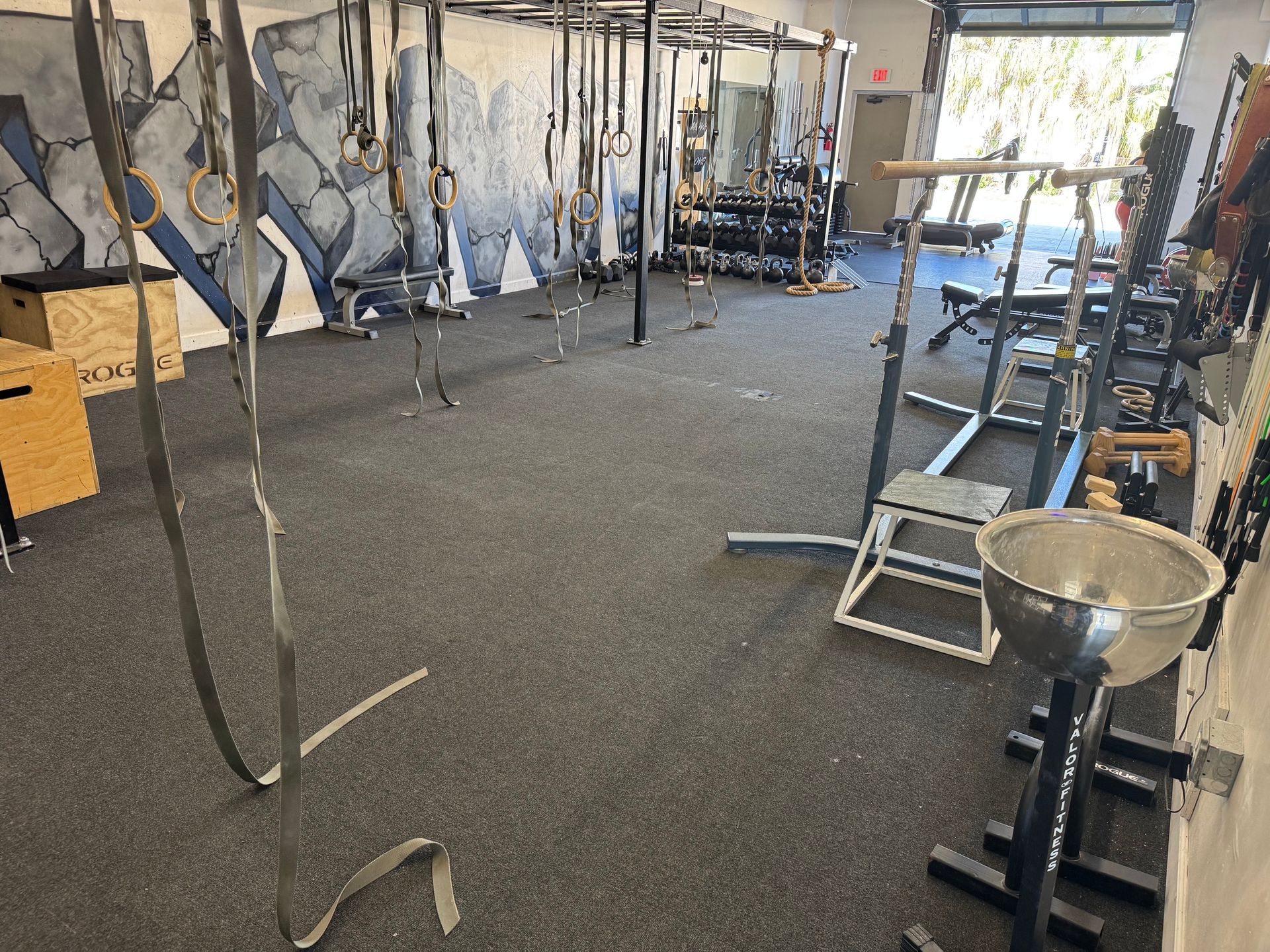 Inside a gym with pull-up rigs, benches, and weightlifting equipment on a rubber floor.