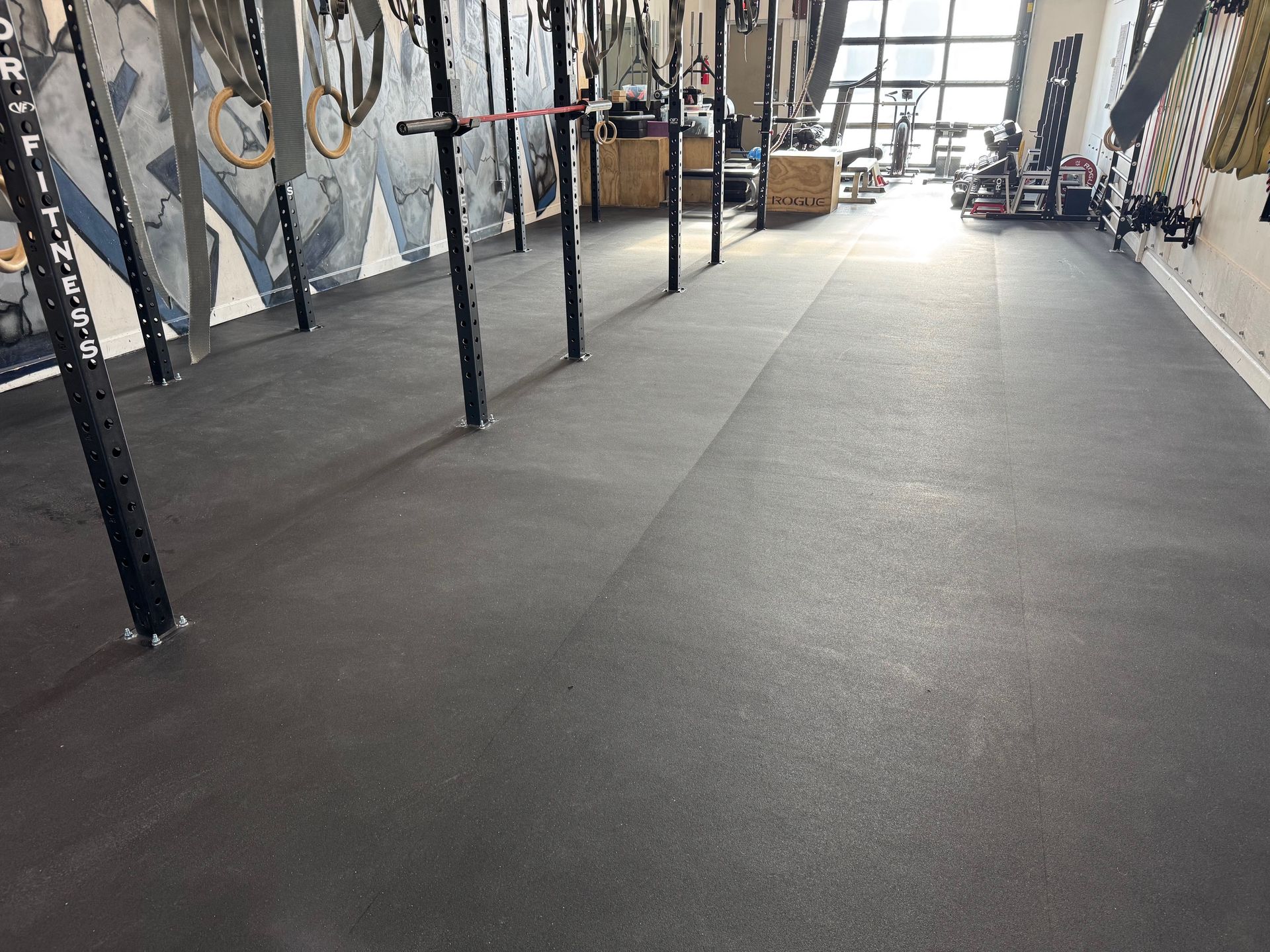 Empty gym with black rubber flooring and exercise rigs along the walls