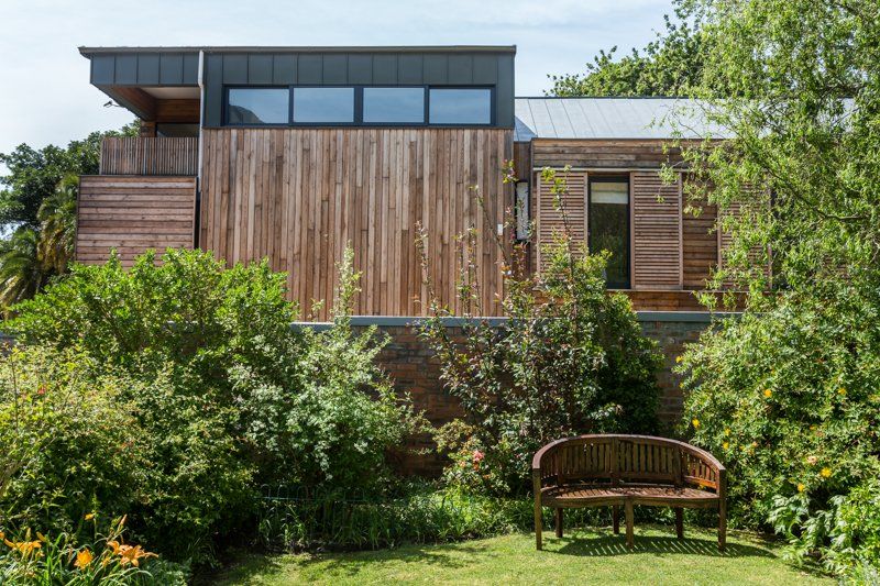A wooden bench is sitting in front of a wooden house surrounded by trees and bushes. 7 Lemon Lane – Newlands