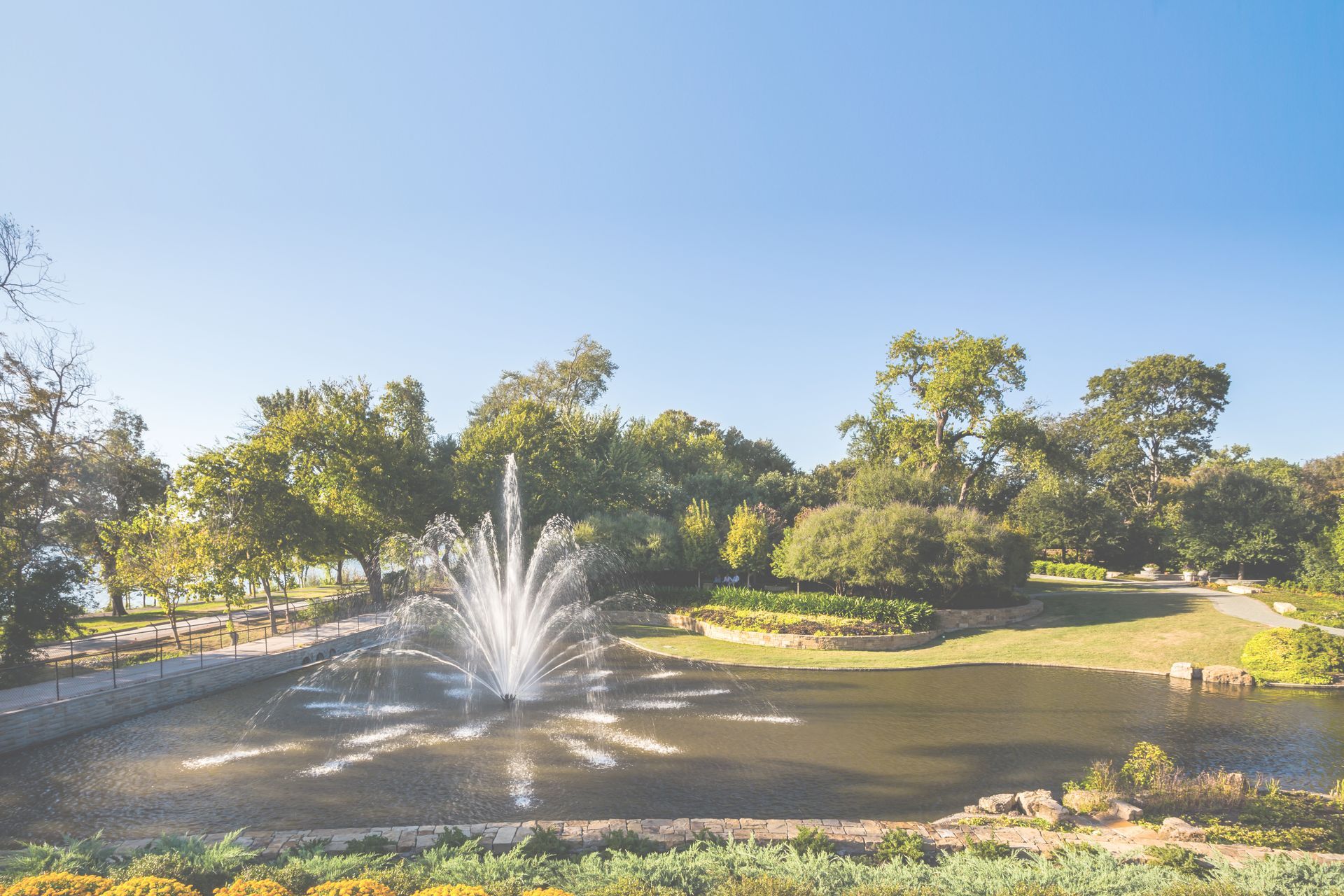 A fountain in the middle of a pond in a park surrounded by trees.