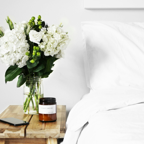 A vase of white flowers sits on a wooden table next to a candle