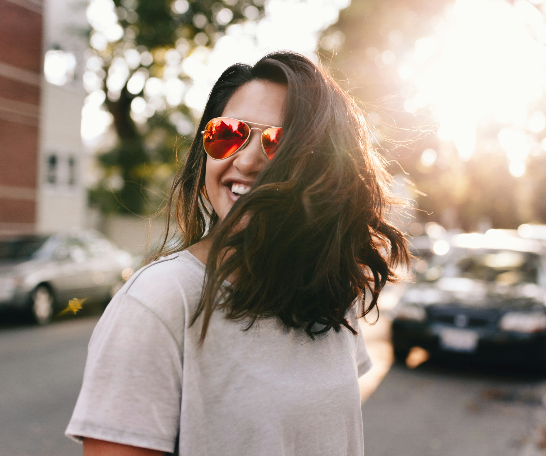 A woman wearing sunglasses is smiling while standing on a street.