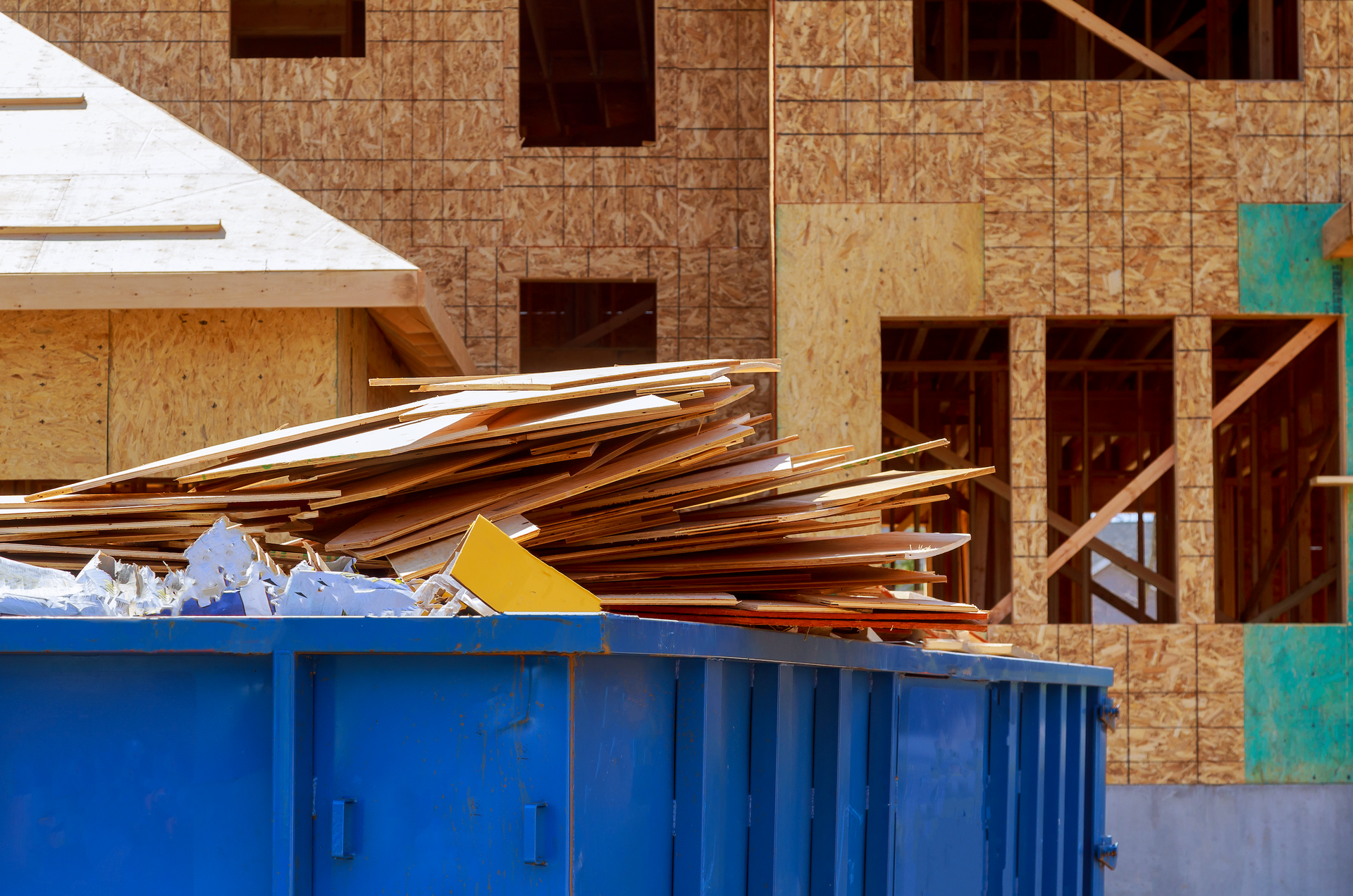Blue dumpster filled with construction debris, in front of a building under construction.