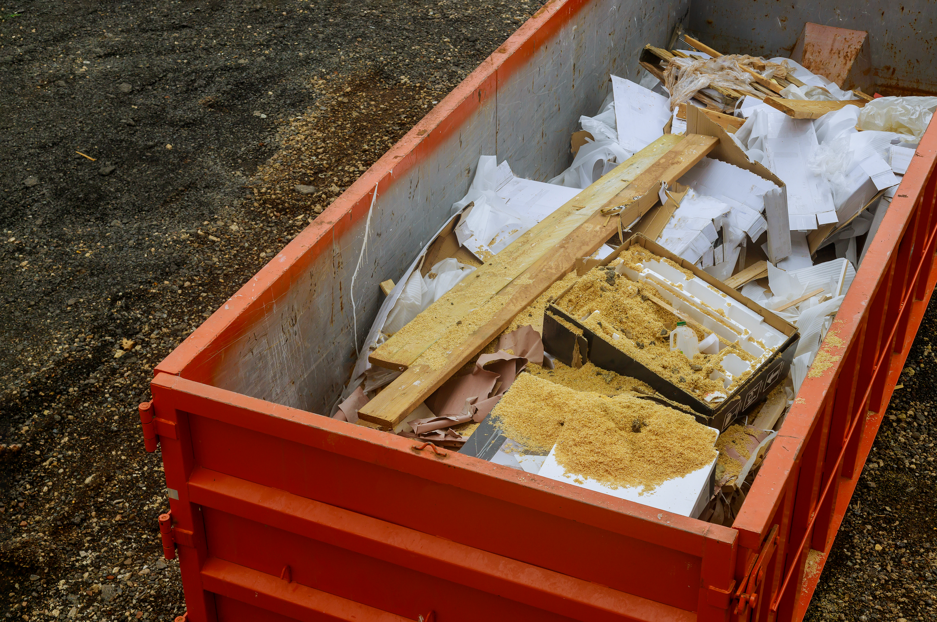 Orange dumpster filled with construction debris, including wood and insulation.