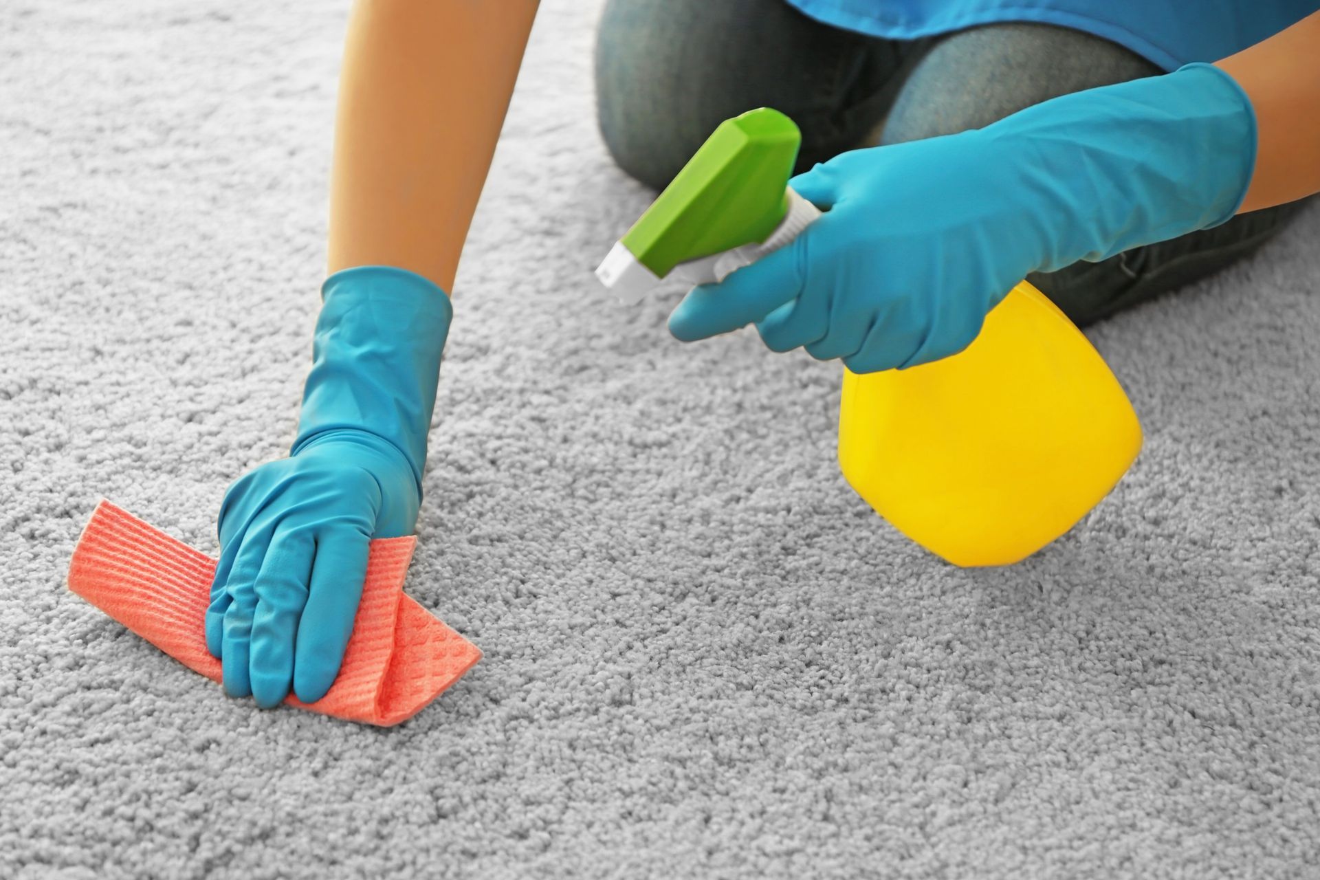 A person is cleaning a carpet with a spray bottle and a cloth.