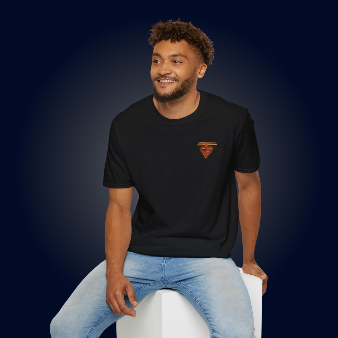 Man in black t-shirt and blue jeans smiles, sitting on a white cube, against a dark blue background.