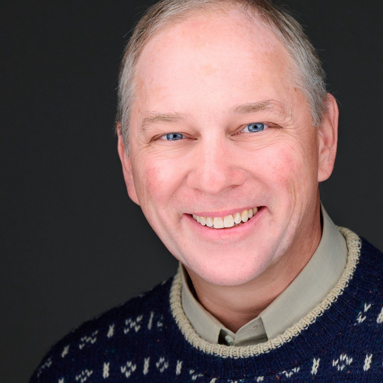 A man wearing a blue sweater is smiling for the camera
