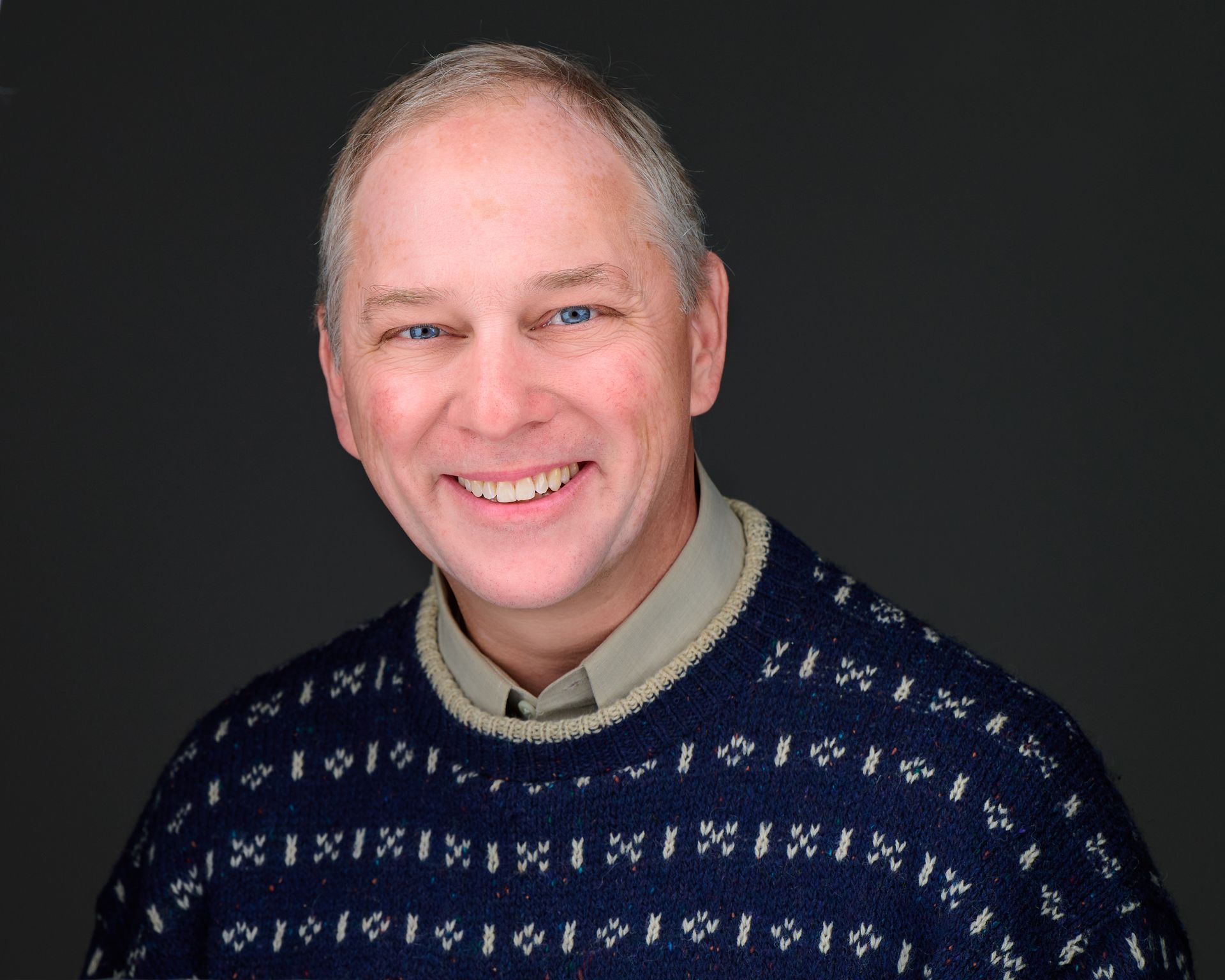 A man wearing a blue sweater is smiling for the camera