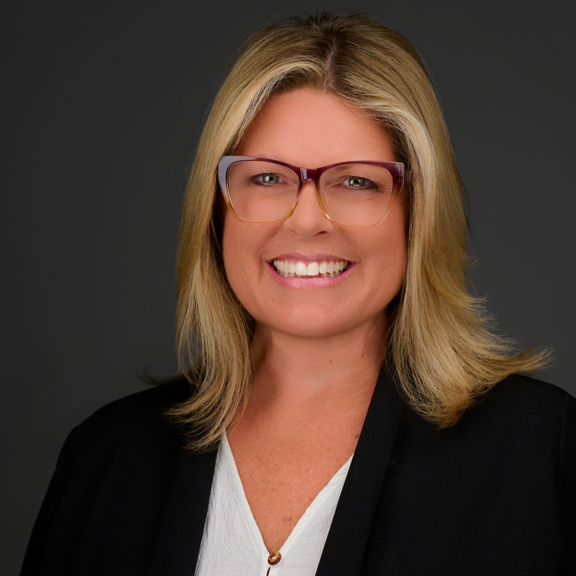 A woman wearing glasses and a black jacket is smiling for the camera.