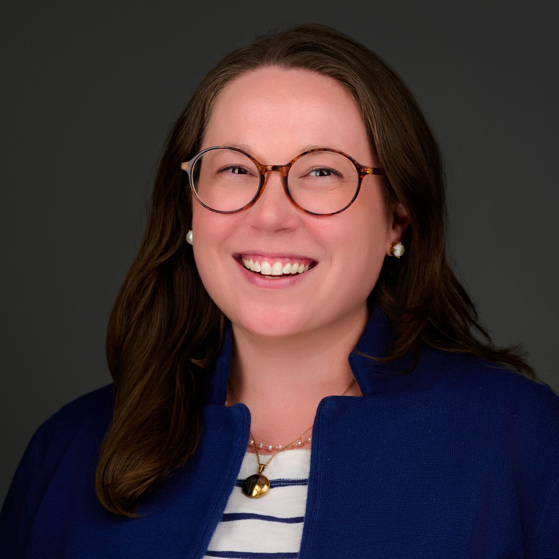 A woman wearing glasses and a blue jacket is smiling.