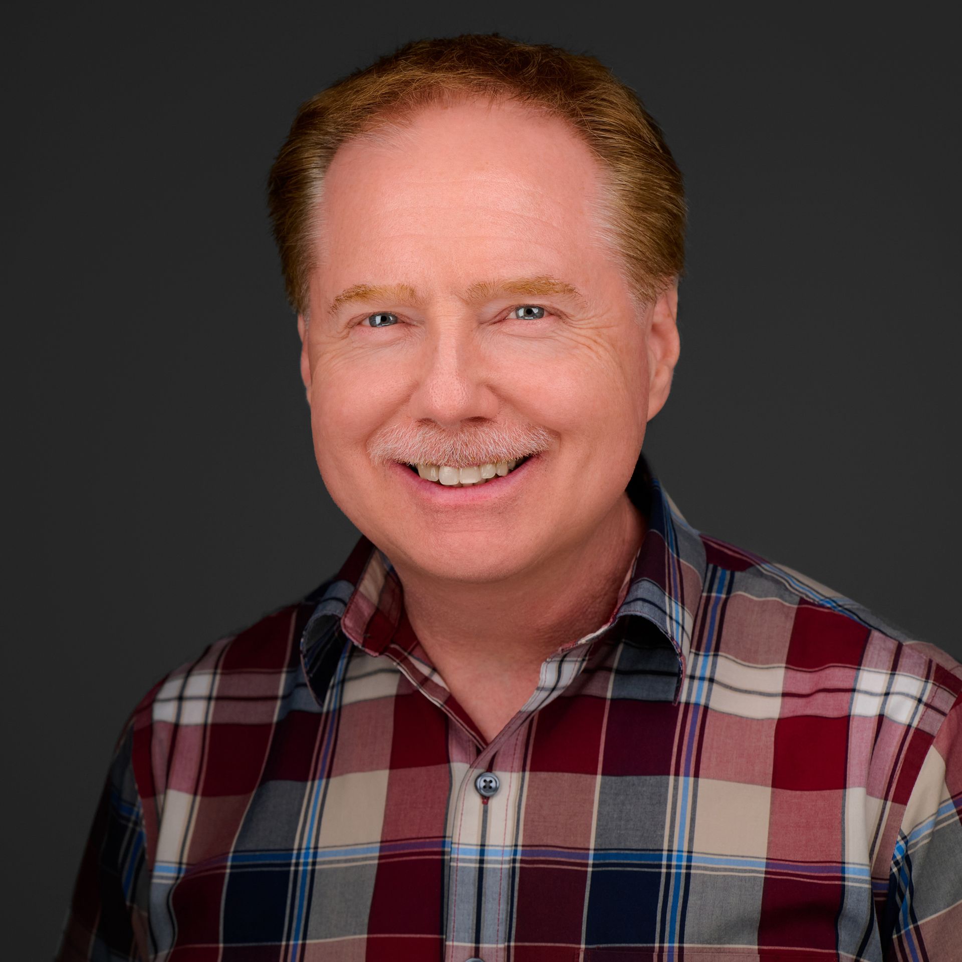 A man in a plaid shirt is smiling for the camera.