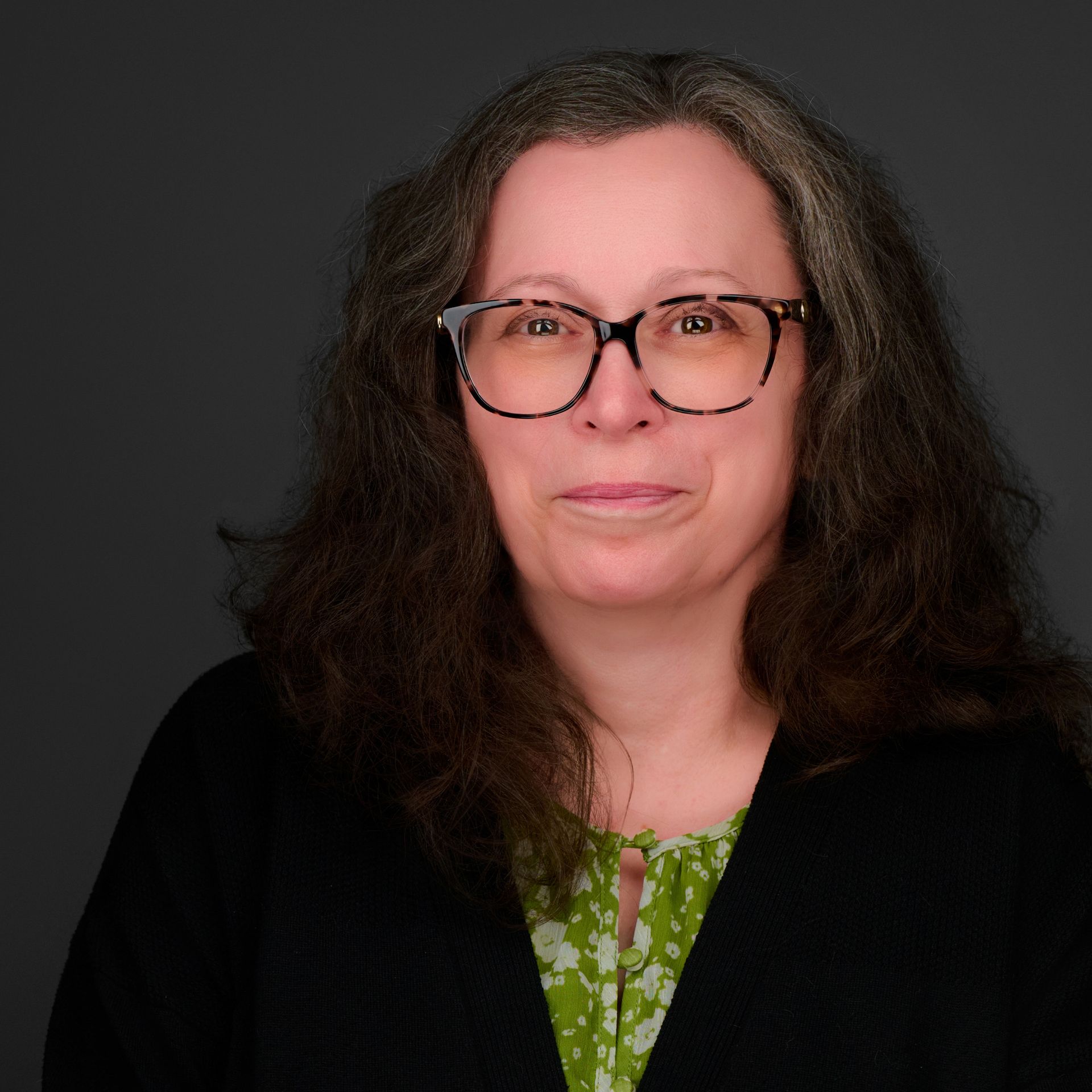 A woman wearing glasses and a black jacket is smiling for the camera.
