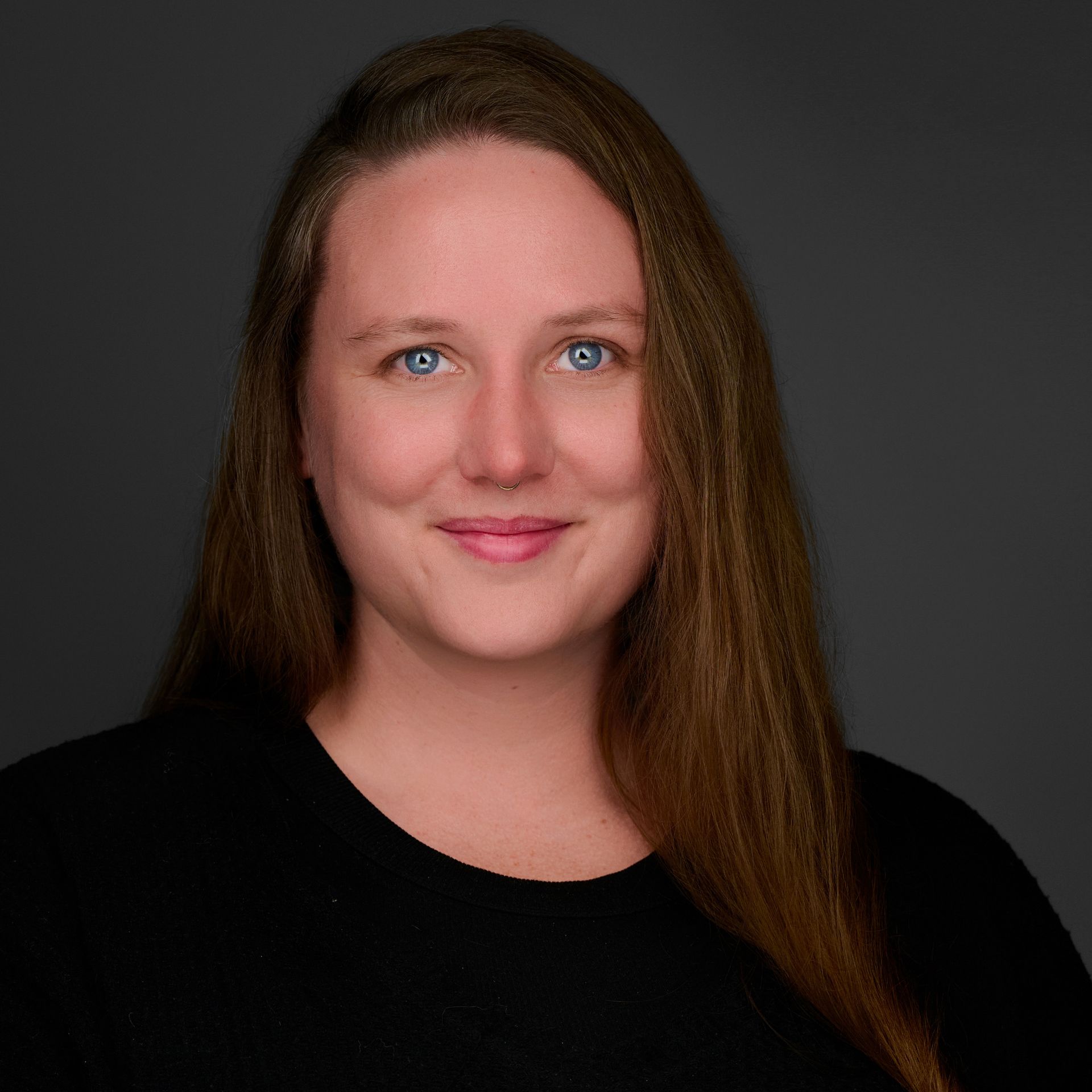 A woman with long brown hair and blue eyes is wearing a black shirt.