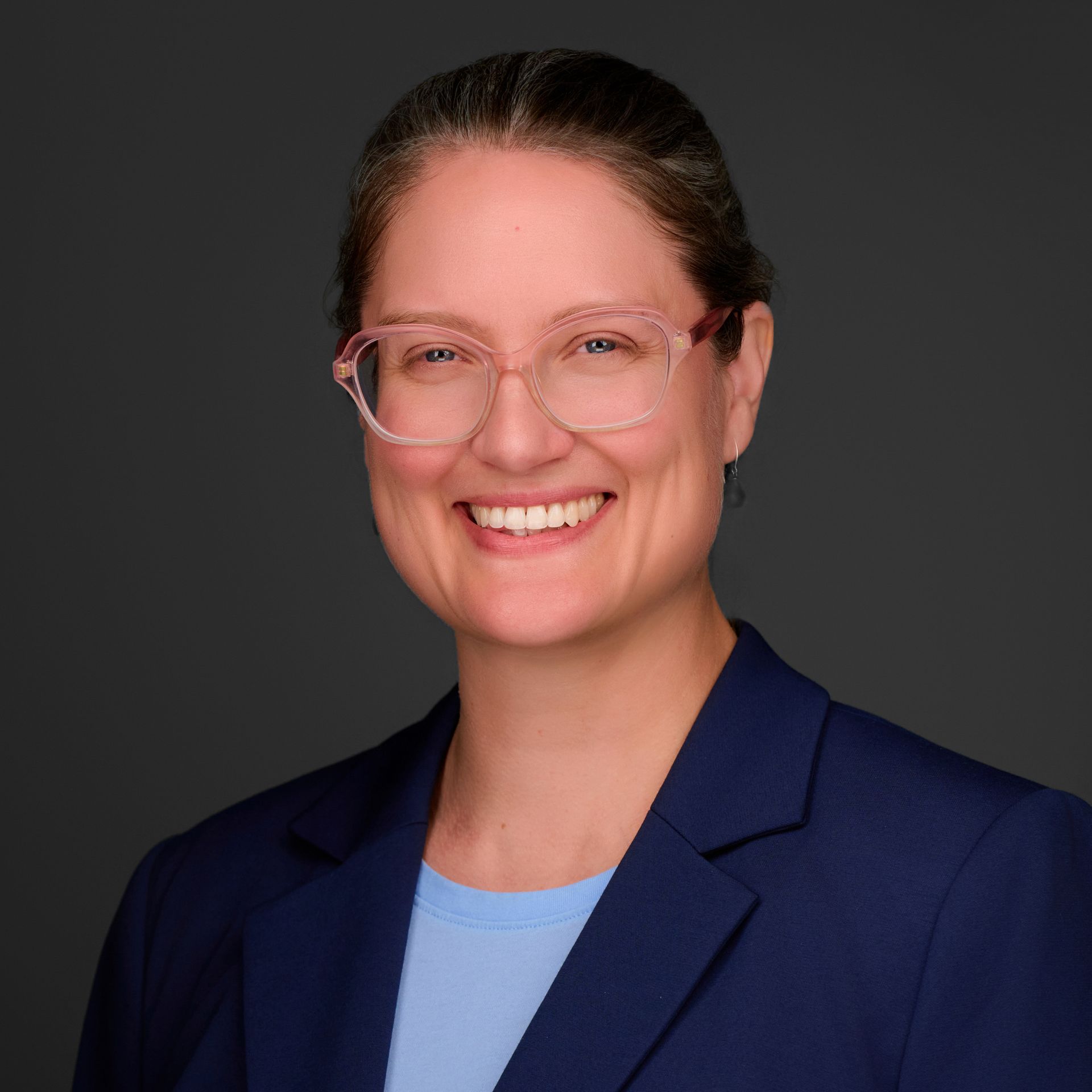 A woman wearing glasses and a blue jacket is smiling for the camera.