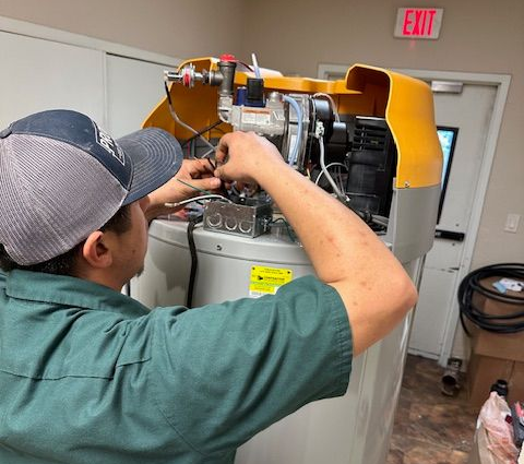 Person in green shirt and hat working on a water heater, indoors.