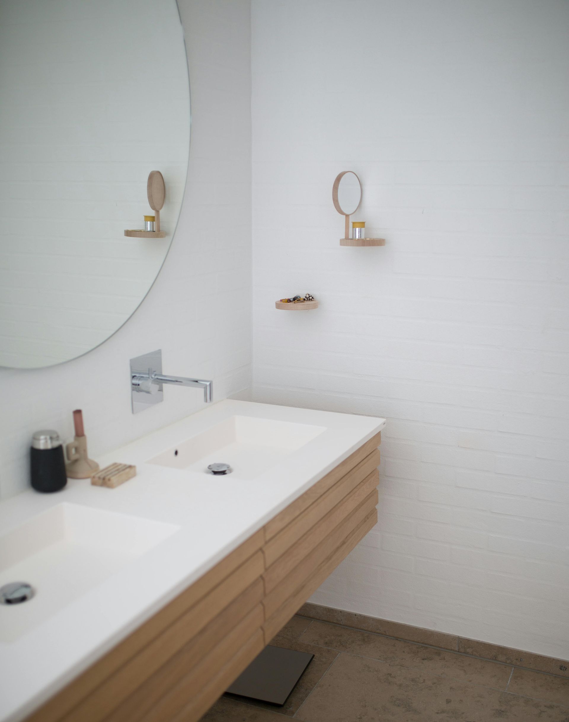 Bathroom with a white sink, wooden cabinets, and a large round mirror.