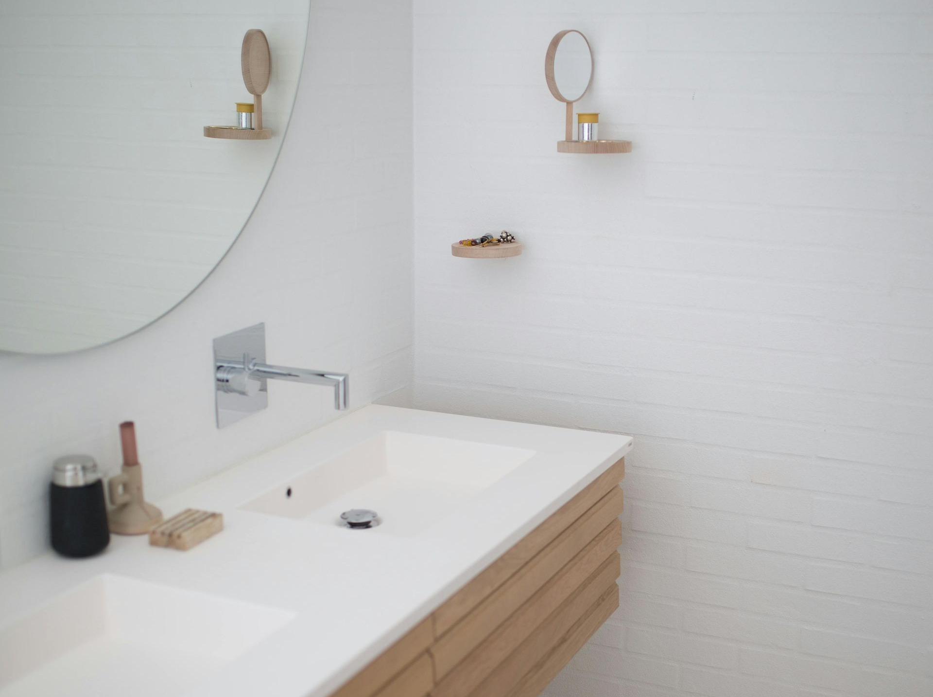 Modern bathroom with large mirror over white sink and wooden vanity. Small mirror and shelf on wall.