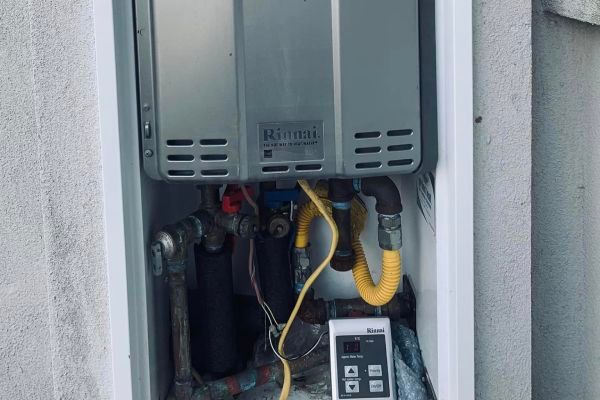 A gas water heater is sitting inside of a box on the side of a building.