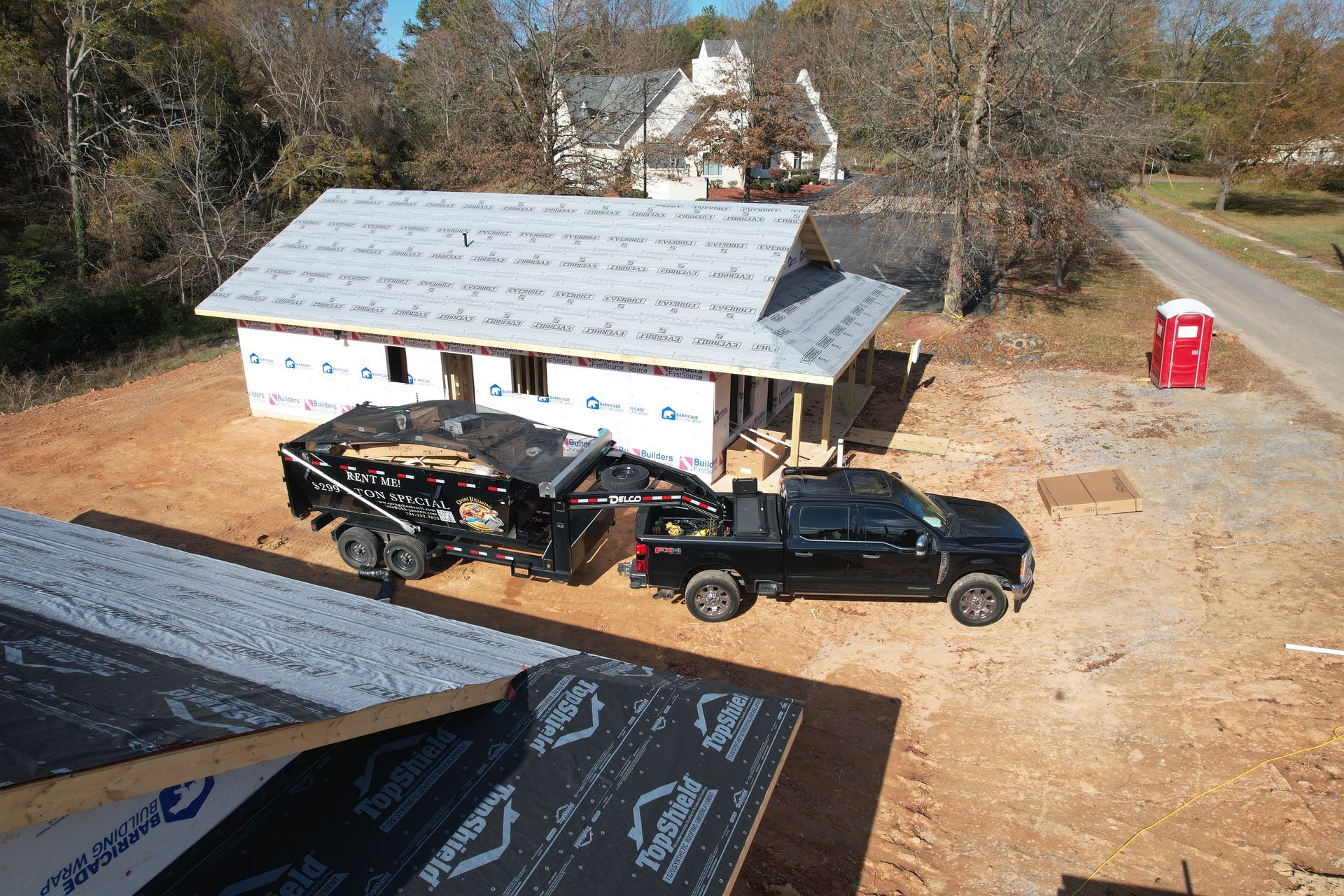A dumpster is parked in front of a house under construction.