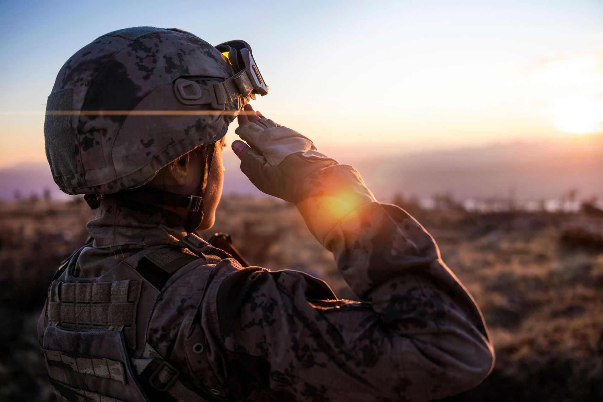 A soldier is saluting the sun while standing in the desert.