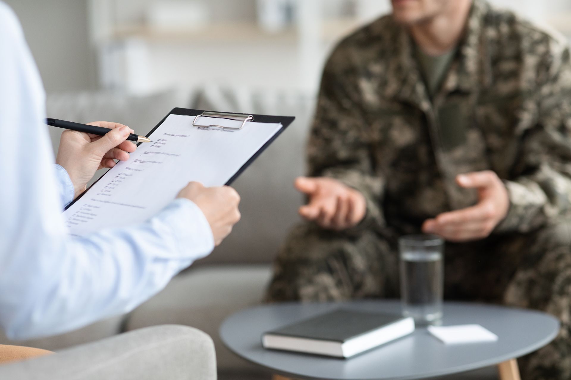 Therapist taking notes during a counseling session with a seated client in camouflage uniform