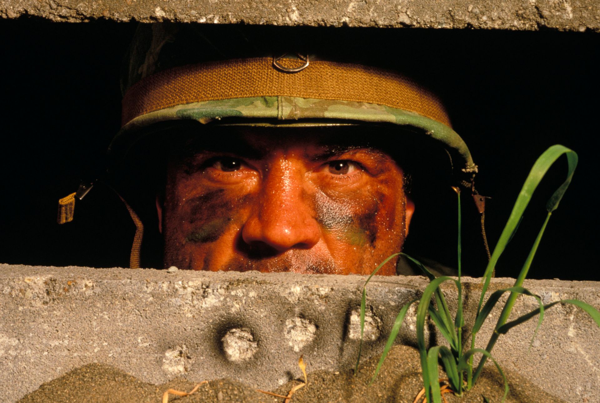 Soldier peering through a concrete bunker opening, wearing a helmet in warm light